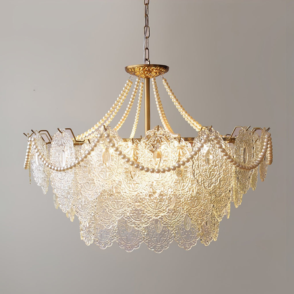 This Clérachic pendant light, lit and hanging on a chain, with glass panels in a stepped shape and pearl swags against a grey wall.