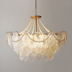 This Clérachic pendant light, lit and hanging on a chain, with glass panels in a stepped shape and pearl swags against a grey wall.