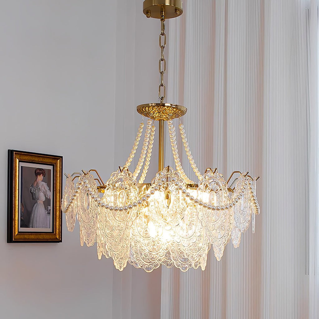 Lit Clérachic pendant hanging on a thin chain beside a framed portrait, with pearl strands over gold arms and clear glass panels.