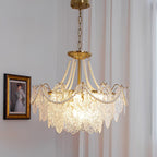 Lit Clérachic pendant hanging on a thin chain beside a framed portrait, with pearl strands over gold arms and clear glass panels.