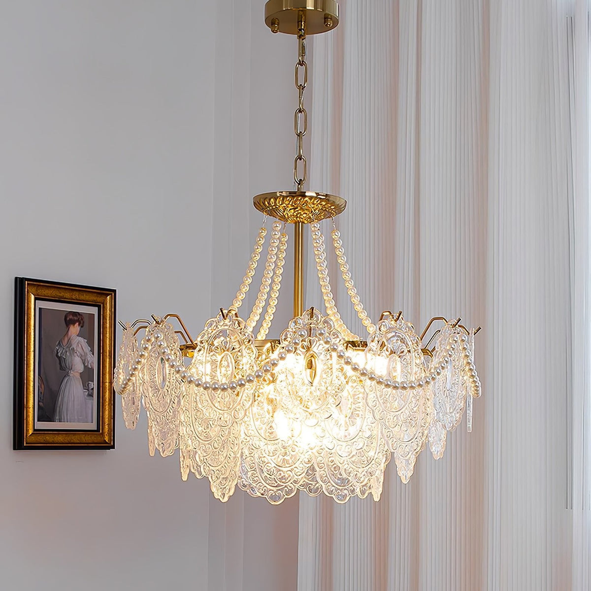 Lit Clérachic pendant hanging on a thin chain beside a framed portrait, with pearl strands over gold arms and clear glass panels.