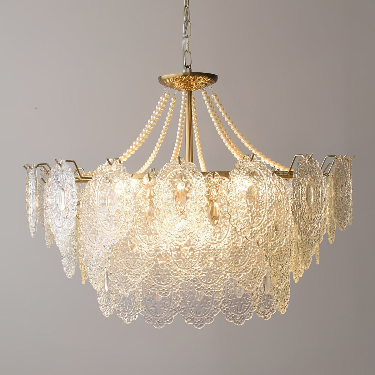 Clérachic pendant light with wide embossed glass panels and short pearl strands, lit against a plain grey wall on a gold-finish chain.