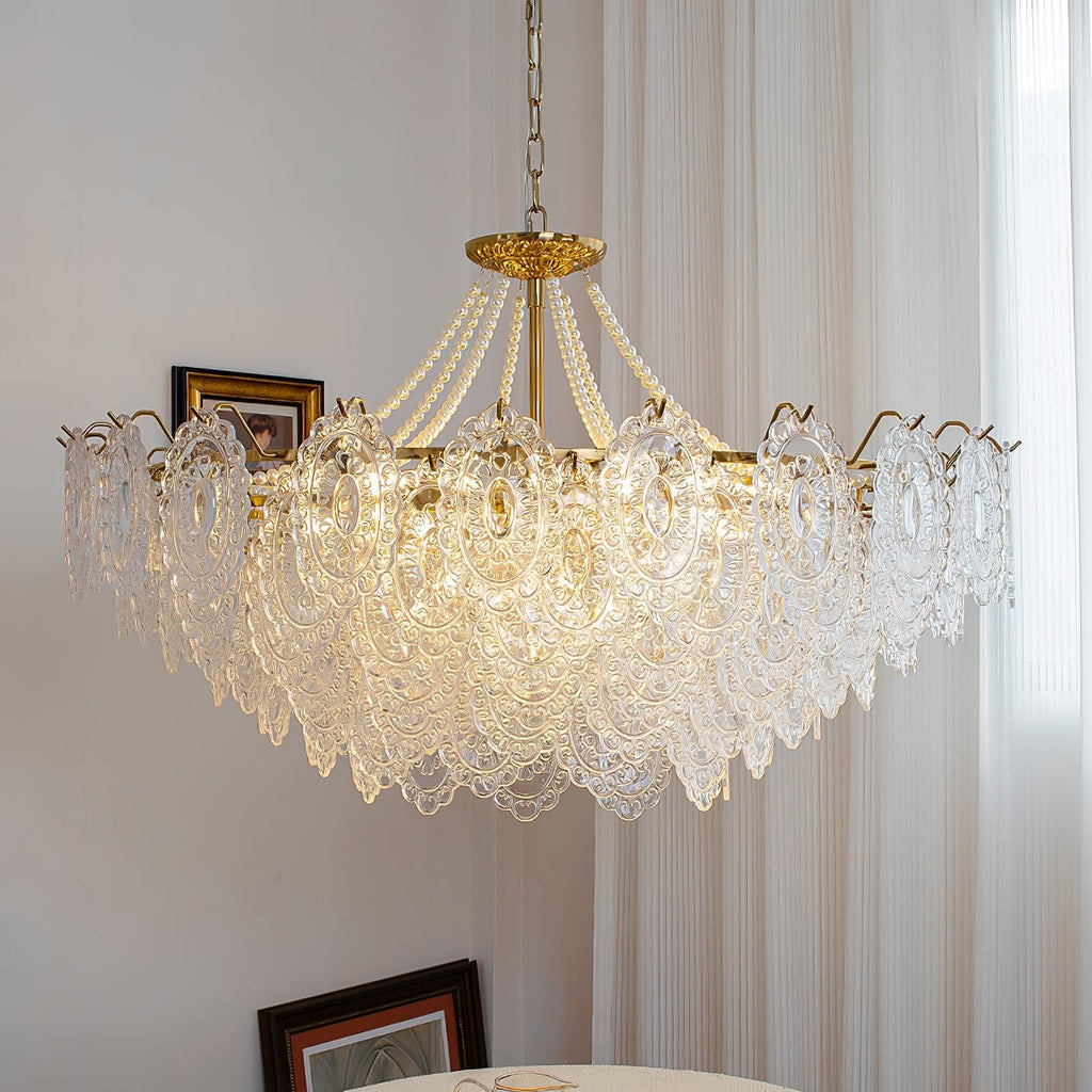 Low-angle view of a wide Clérachic pendant light with layered glass petals, lit beside a sheer curtain and a picture frame.