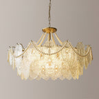 Straight-on view of the lit Clérachic pendant, with its tiers of embossed clear glass and loops of pearl strands on a plain wall.