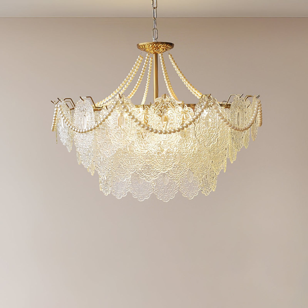 Smaller-looking Clérachic pendant with a rounded skirt of embossed glass and pearl swags, lit against a plain warm-grey wall.