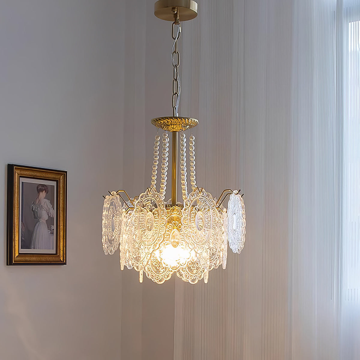 Clérachic pendant with a shorter, straighter glass skirt and pearl strands, lit beside a gilt-framed portrait and a sheer curtain.