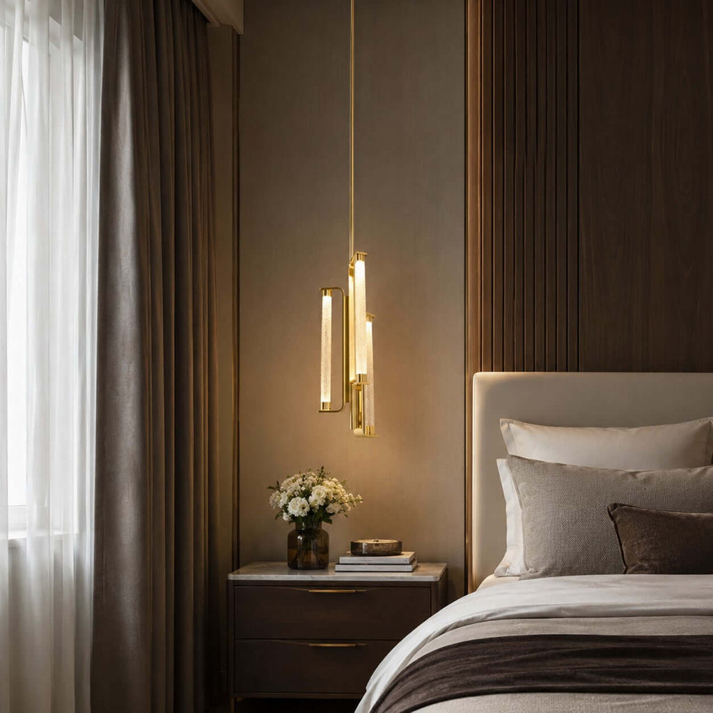 A Clérachic brass pendant lit warm beside a bed with a pale headboard, in front of a dark wood panel and a grey curtain.