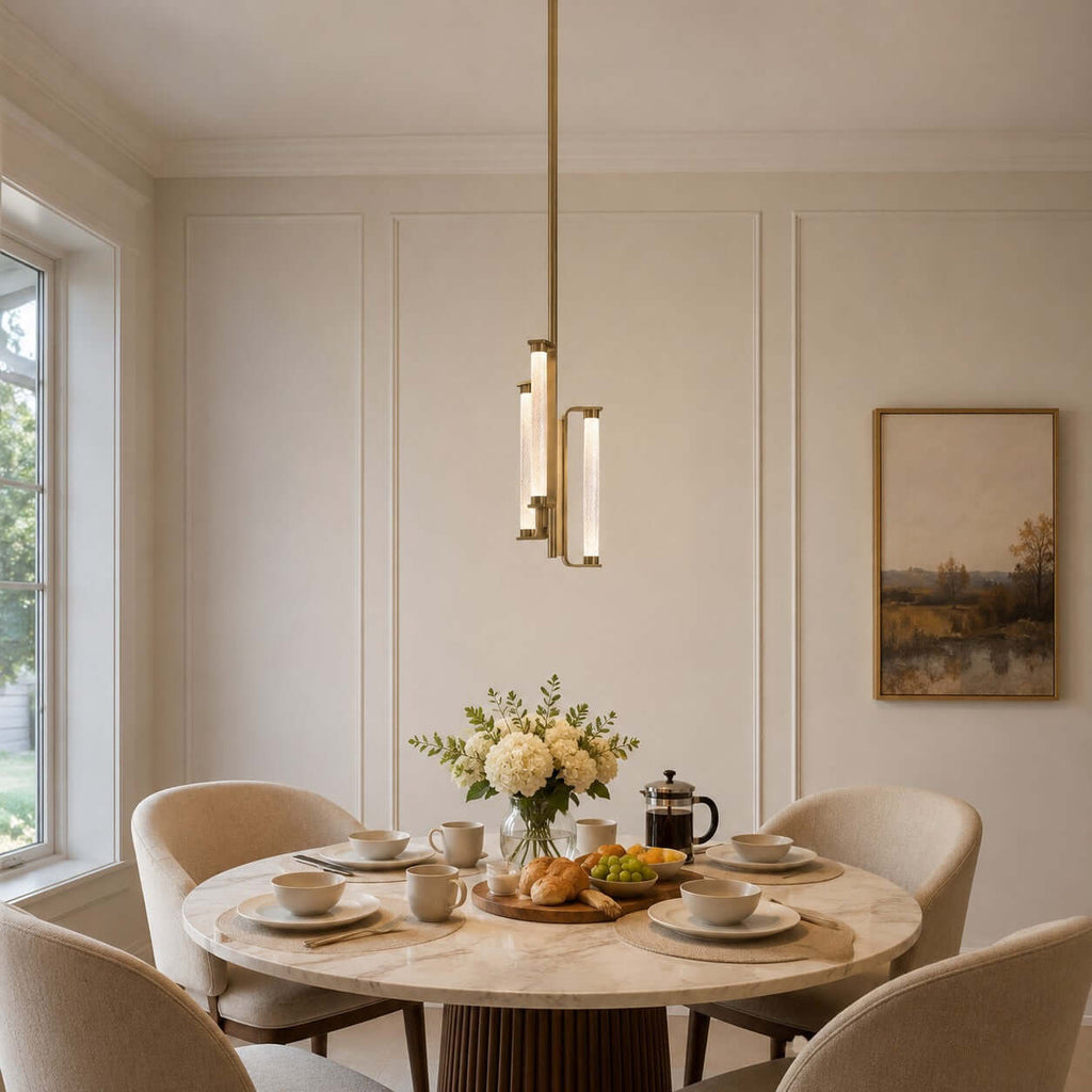 A Clérachic brass and glass pendant hangs above a round marble breakfast table set with croissants, coffee cups and fresh flowers.