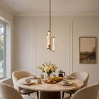 A Clérachic brass and glass pendant hangs above a round marble breakfast table set with croissants, coffee cups and fresh flowers.