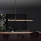 A Clérachic glass tube pendant lit above a dark dining table, hung from two brown leather straps against a dark slatted wall.