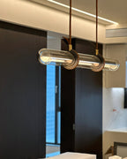 Side-on close view of a Clérachic glass tube pendant, with leather loops around the clear glass and a brass fitting at each strap.