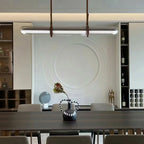 A Clérachic glass tube pendant over a dark dining table, in front of a white relief wall panel and shelves of bottles.