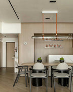 A Clérachic glass tube pendant on tan leather straps over a round-ended dining table in a warm wood-panelled room.