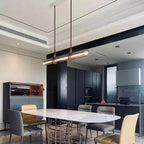 A Clérachic glass tube pendant at a slight angle above a marble-topped dining table in a modern kitchen with dark units.