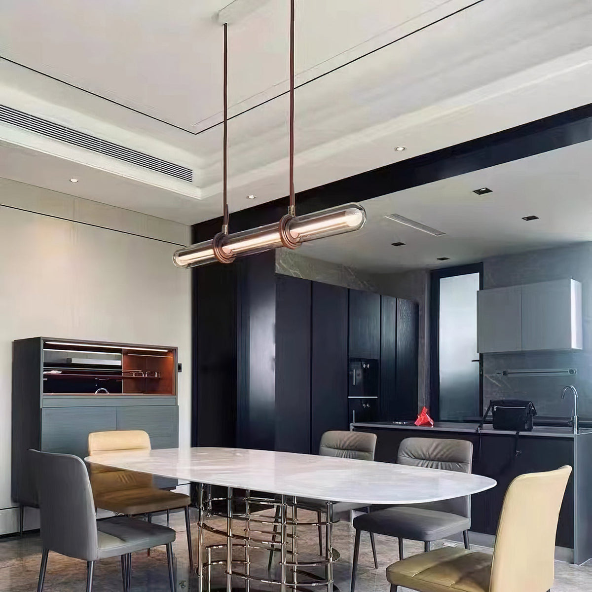 A Clérachic glass tube pendant at a slight angle above a marble-topped dining table in a modern kitchen with dark units.