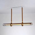 A Clérachic glass tube pendant on tan leather straps from a white ceiling plate, glowing warm against a plain white wall.