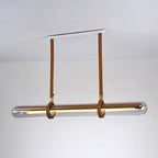 A Clérachic glass tube pendant on tan leather straps from a white ceiling plate, glowing warm against a plain white wall.