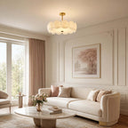 Brass-stemmed Clérachic pendant of layered white glass discs above a coffee table in a cream living room with pink curtains.