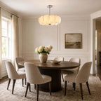 Chrome-stemmed Clérachic glass-disc pendant over a round walnut dining table, with six upholstered chairs and white hydrangeas.