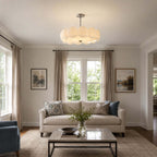 Clérachic pendant with a chrome stem above a living room with a linen sofa, a glass coffee table and two framed prints.