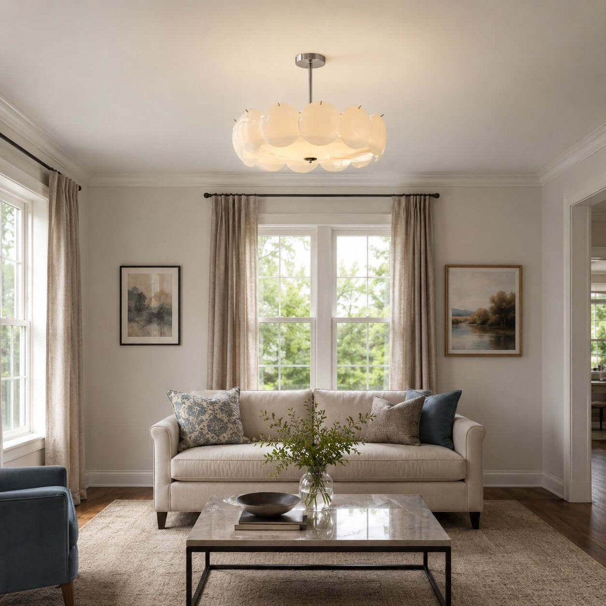 Clérachic pendant with a chrome stem above a living room with a linen sofa, a glass coffee table and two framed prints.