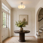 Small Clérachic pendant glowing in an entrance hall with an arched doorway, a round dark wood table and a vase of greenery.