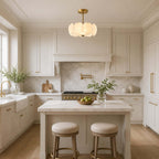 Brass Clérachic pendant above a marble-topped kitchen island with two stools, in a cream kitchen with brass cabinet handles.