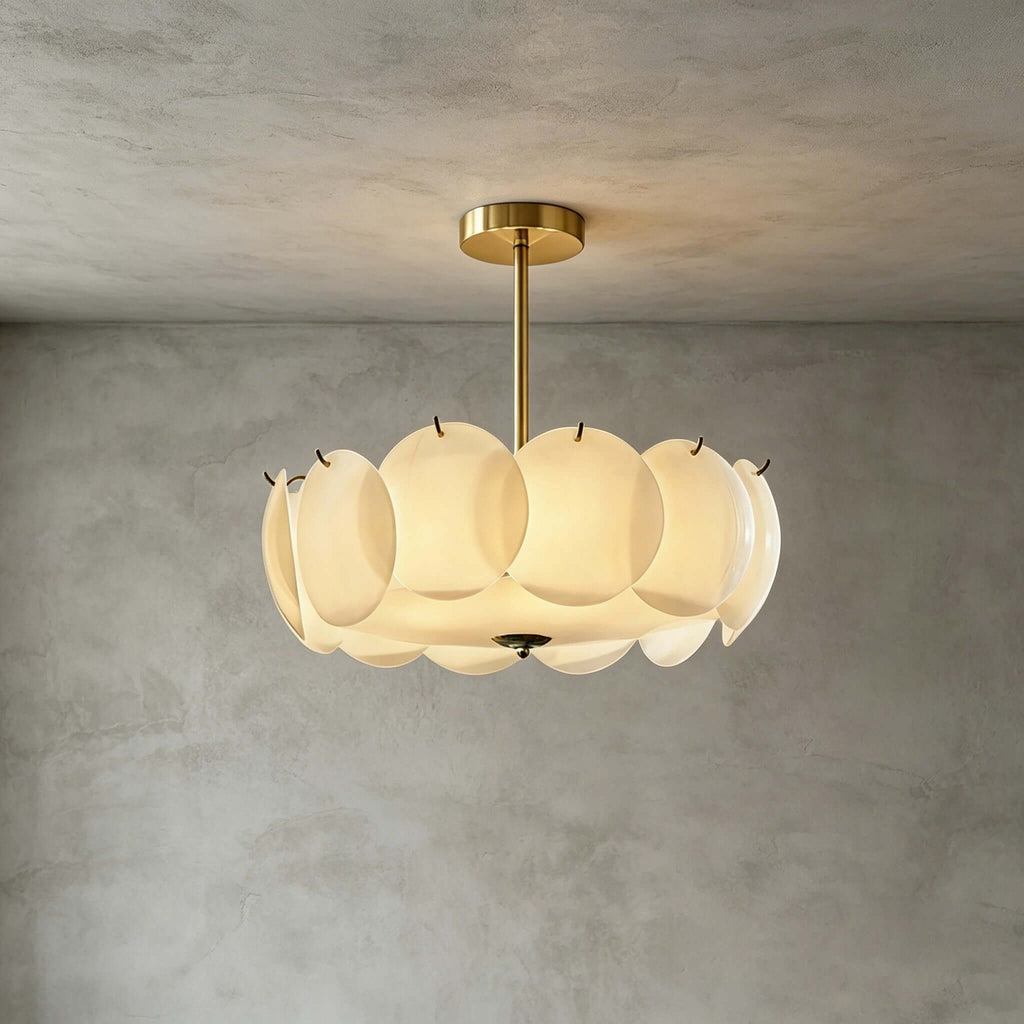 Brass-finish Clérachic pendant of white glass discs hung against a grey plaster wall, with a soft glow from within.
