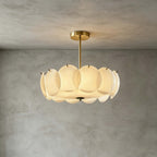Brass-finish Clérachic pendant of white glass discs hung against a grey plaster wall, with a soft glow from within.