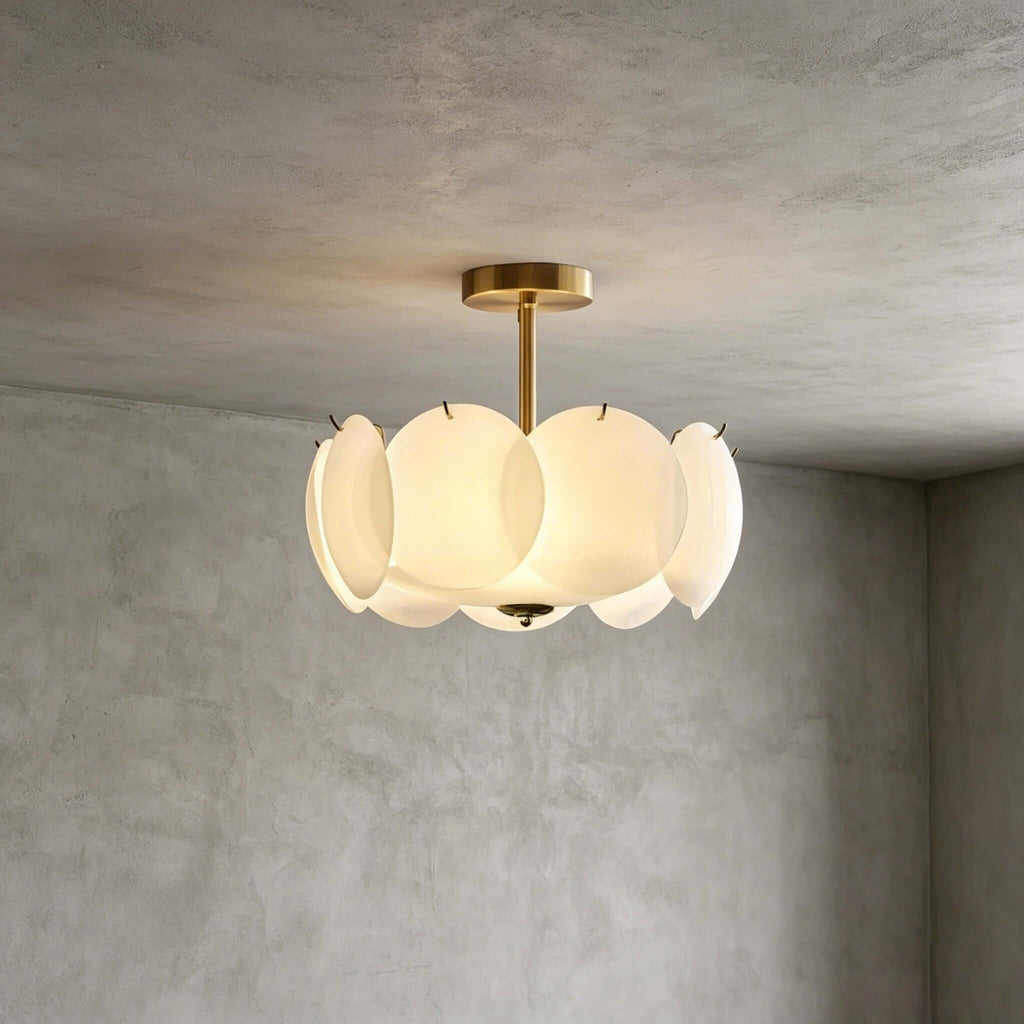 Brass-finish Clérachic pendant seen from a slightly lower angle against grey plaster, its glass discs lit pale gold.