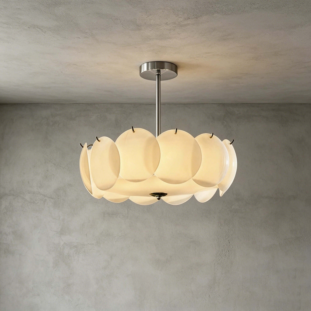 Chrome-finish Clérachic pendant of white glass discs against a grey plaster wall and ceiling, lit and viewed straight on.