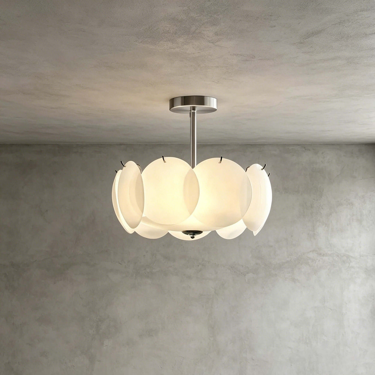 Smaller chrome Clérachic pendant with overlapping glass discs, glowing against a textured grey plaster wall.