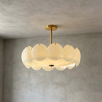 Larger brass-finish Clérachic pendant with a wide ring of white glass discs, lit softly against grey plaster.