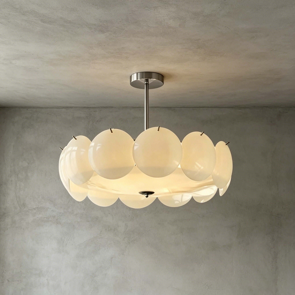 Larger chrome-finish Clérachic pendant with a wide ring of glass discs, glowing against a grey plaster wall.