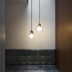 Two small Clérachic glass pendants with gold collars glow above a tufted dark leather banquette and a walnut panel.