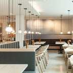 A Clérachic glass pendant hangs in the foreground of a long restaurant interior, among slim cords hanging down to the tables.