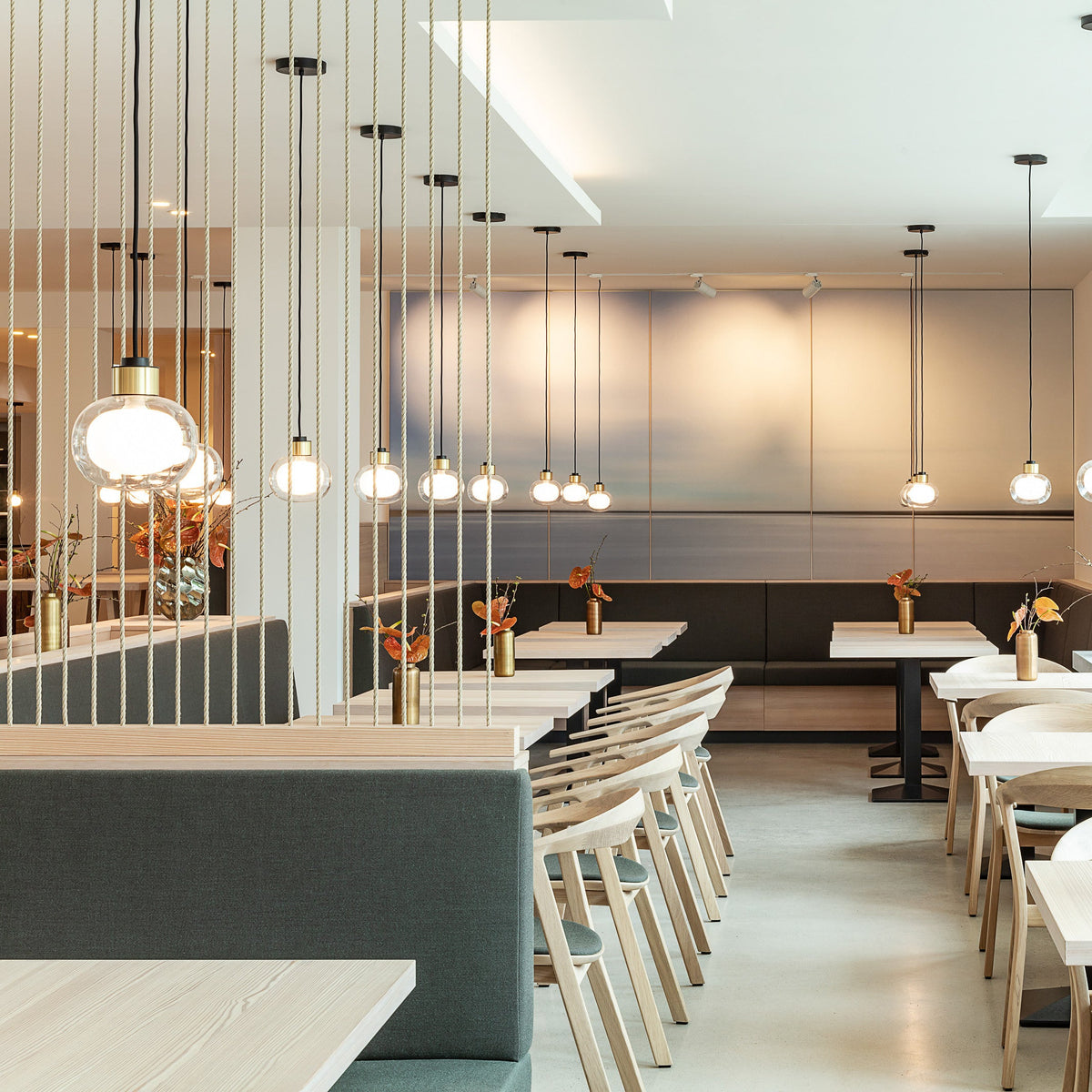 A Clérachic glass pendant hangs in the foreground of a long restaurant interior, among slim cords hanging down to the tables.