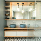 Glass pendants from Clérachic with gold-finish collars hang over a double wooden vanity and blue basins in a bathroom.