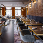 Glass pendants from Clérachic hang in a warm restaurant dining room with amber curtains and tables set for dinner.