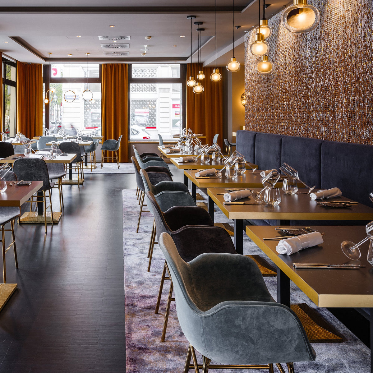 Glass pendants from Clérachic hang in a warm restaurant dining room with amber curtains and tables set for dinner.