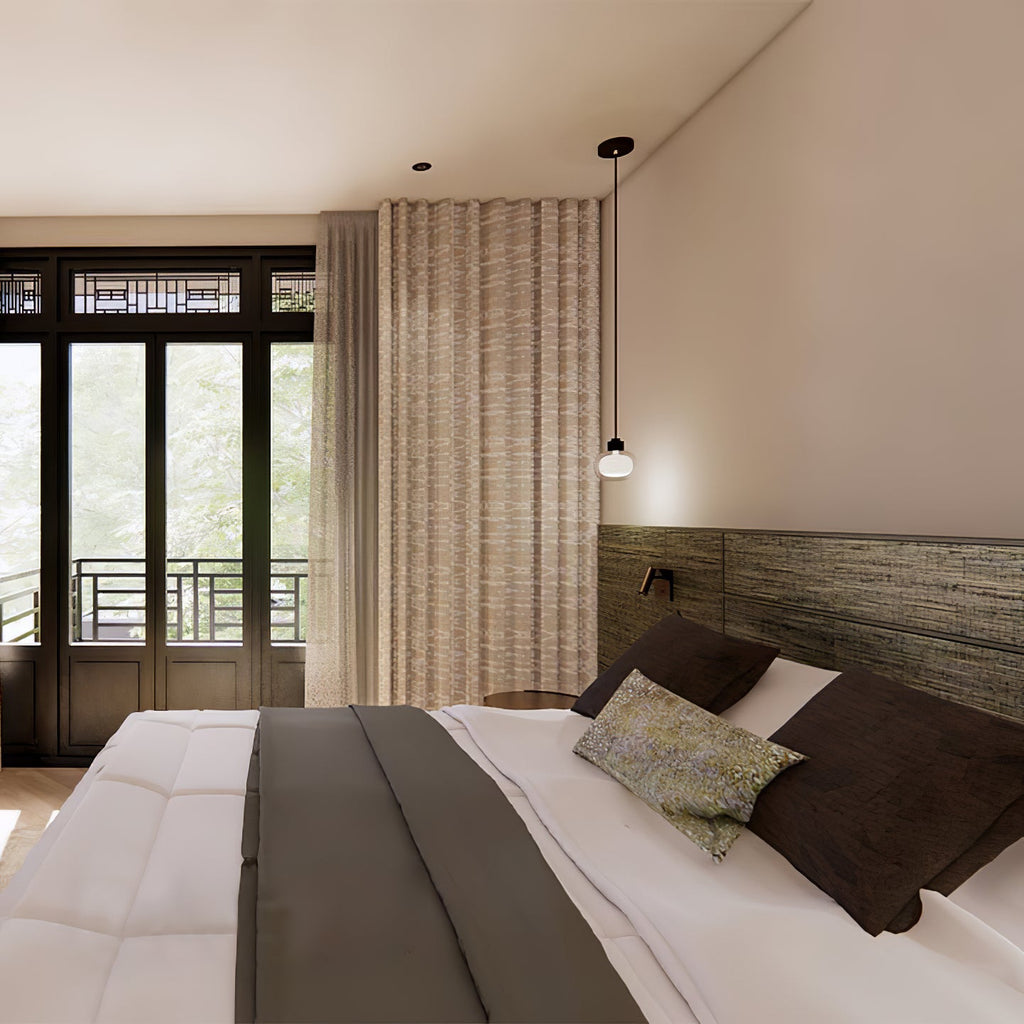 A single Clérachic glass pendant hangs near a tall window in a bedroom, over the foot of a white bed with a grey throw.