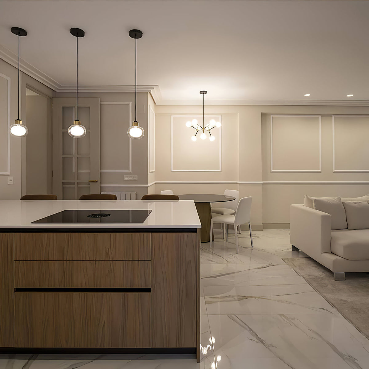 Three Clérachic glass pendants hang over a kitchen island with a wood-fronted base, beside a white marble floor and dining table.