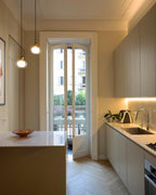 Two Clérachic glass pendants hang in a kitchen with tall French windows and herringbone parquet flooring.