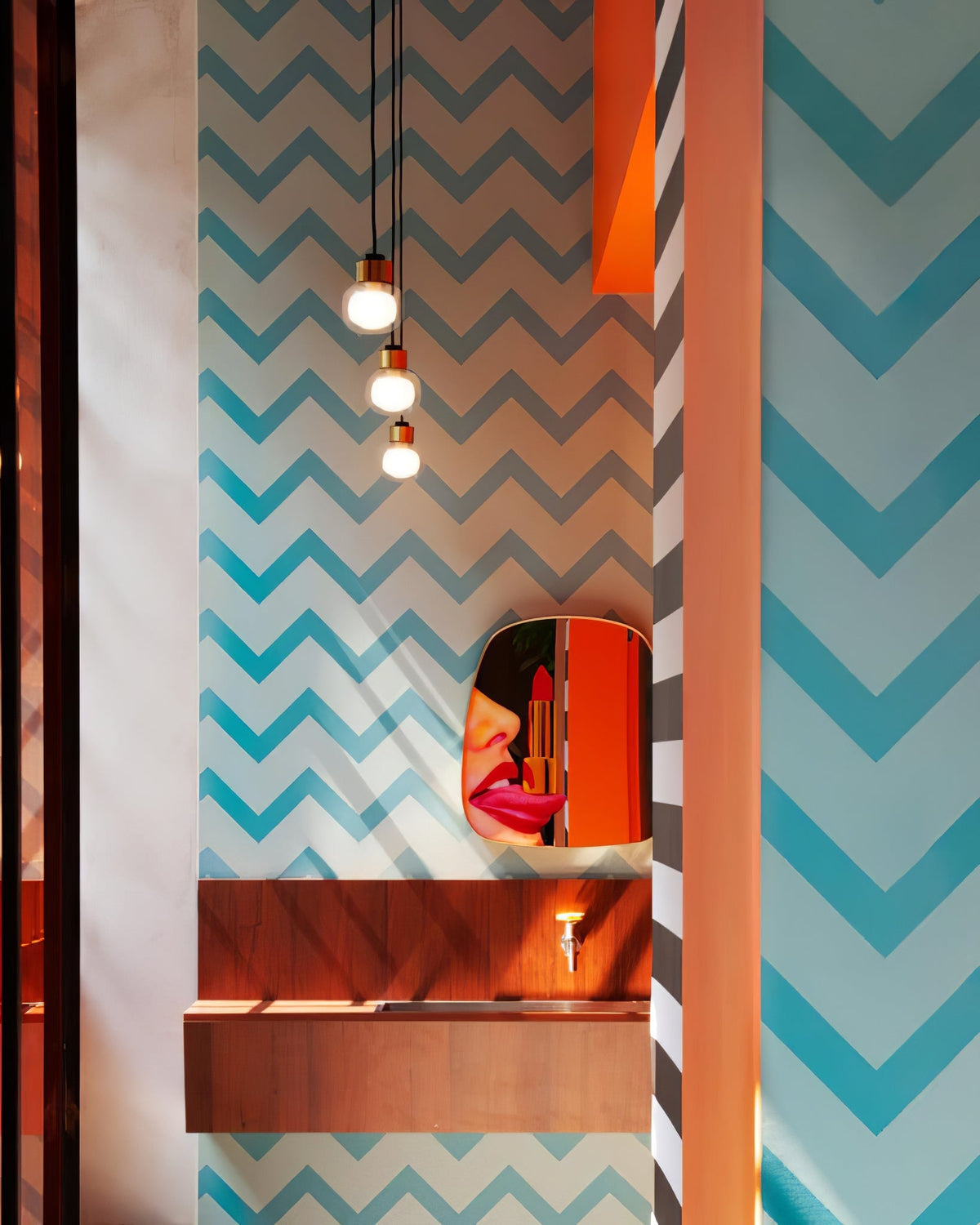 Three Clérachic glass pendants hang in a narrow bathroom with blue chevron wallpaper and a mirror in warm orange tones.