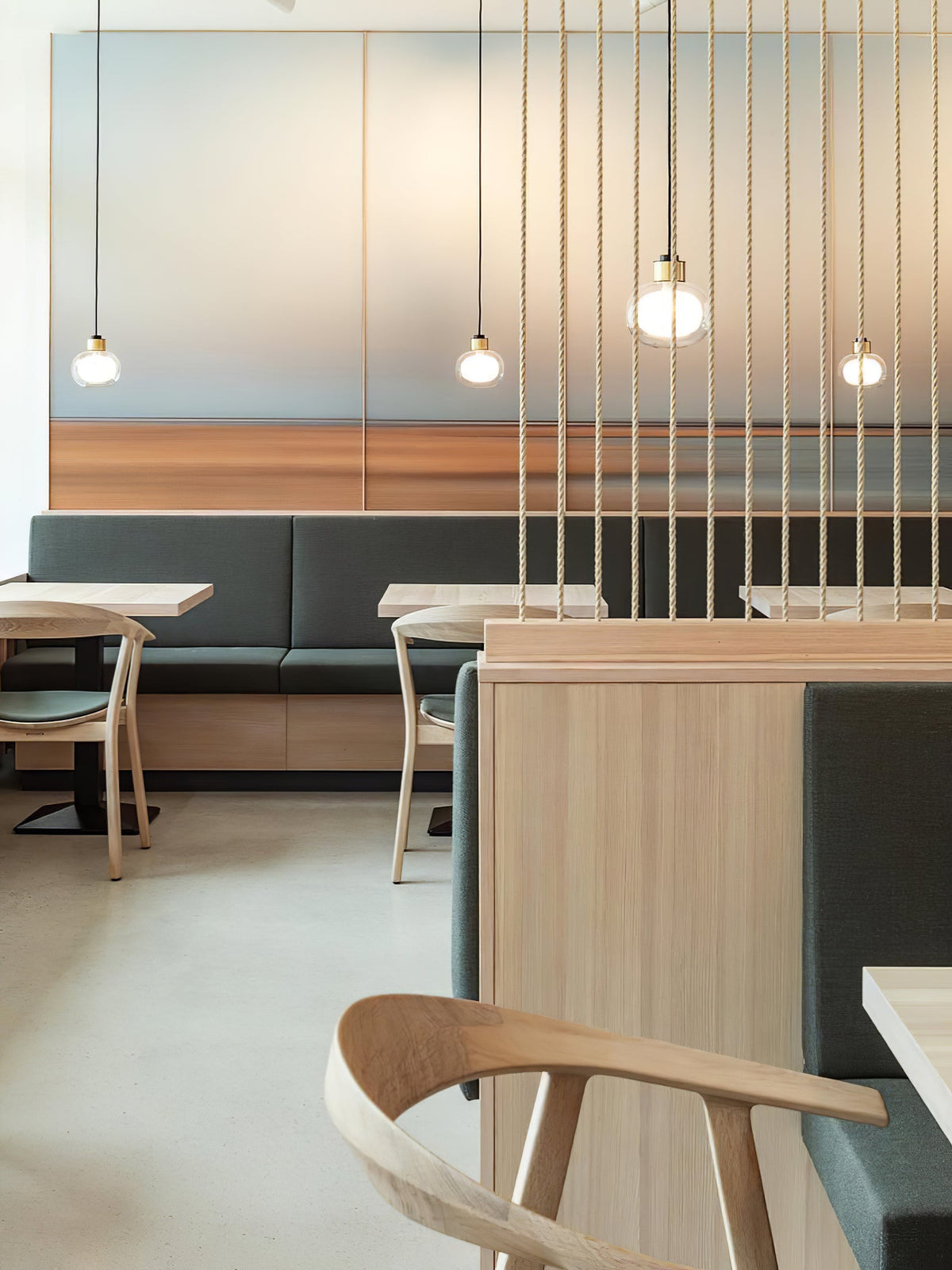 Several Clérachic glass pendants hang at different heights over a restaurant seating area, with slim cords in front of a frosted wall.