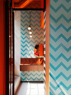 Three Clérachic glass pendants hang in a narrow bathroom with blue chevron wallpaper and an orange-framed corridor.
