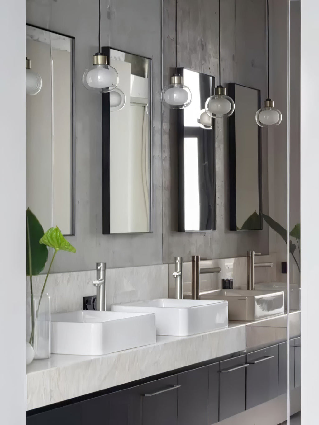 Several glass pendants from Clérachic hang in front of tall mirrors, above two white basins on a marble-topped vanity.
