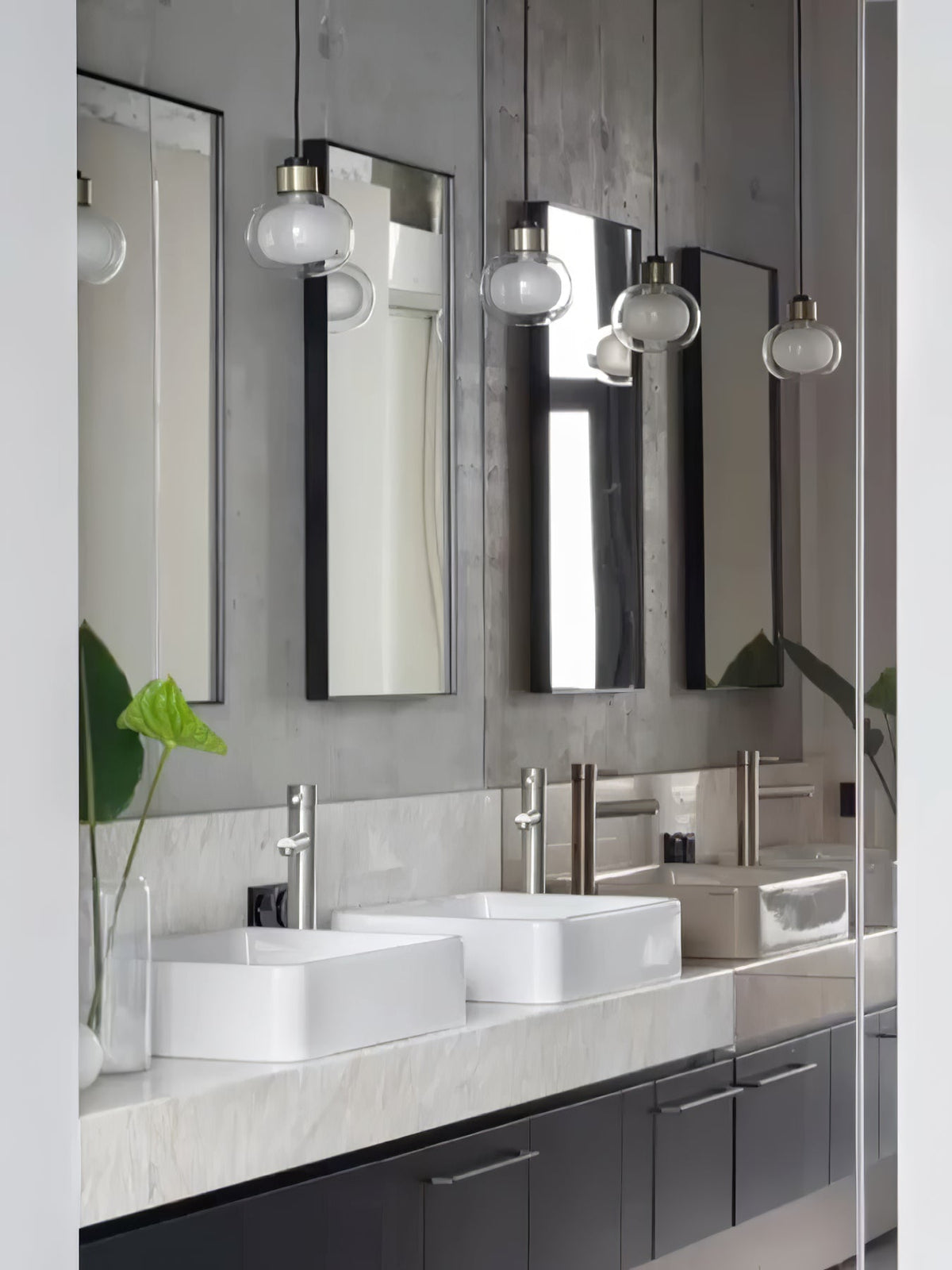 Several glass pendants from Clérachic hang in front of tall mirrors, above two white basins on a marble-topped vanity.