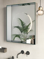 A Clérachic glass pendant with a gold collar hangs beside a green-framed mirror, with a wall-mounted tap and a palm leaf reflected in it.