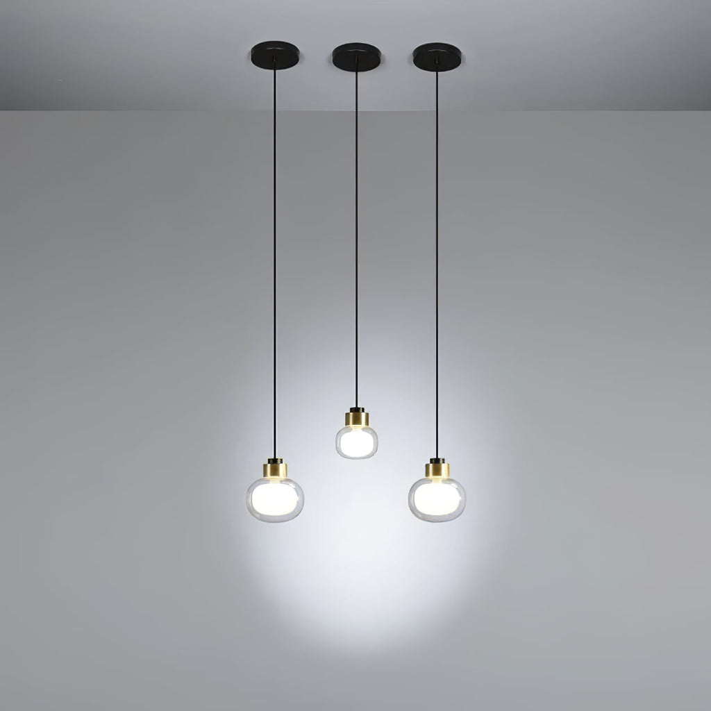 Three Clérachic glass pendants hang at different heights from black ceiling canopies, lighting a plain grey wall.